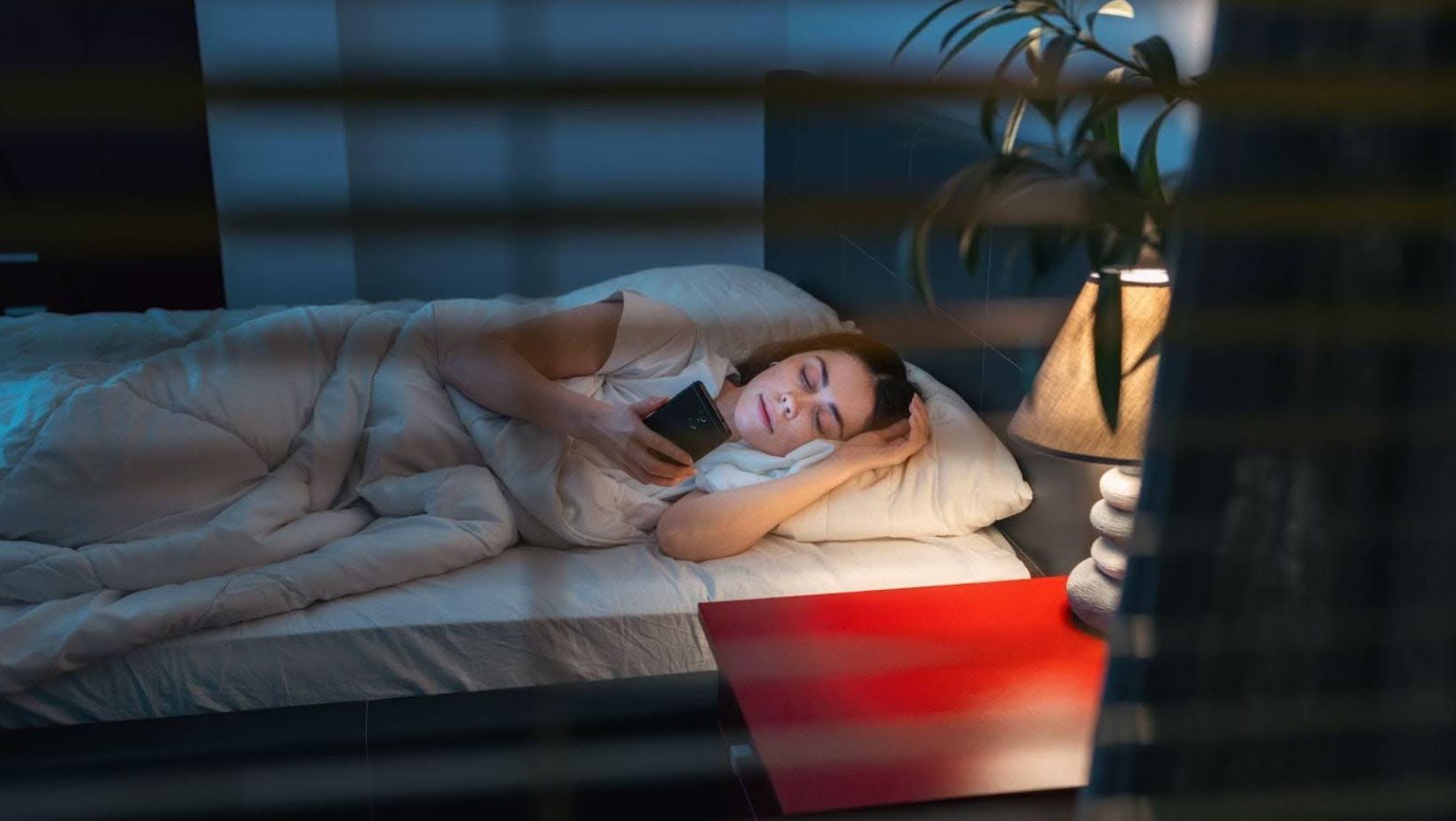 A woman lying in bed looking through someone else's phone and wondering, “Is it illegal to look through someone's phone?